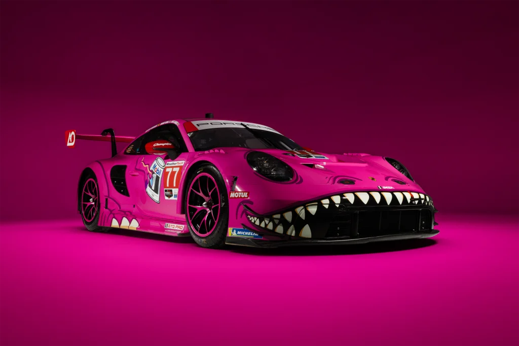 Quelle: www.aoracing.com Rosa Rennsportwagen mit scharfen Zähnen und auffälligem Design auf pinkem Hintergrund.
